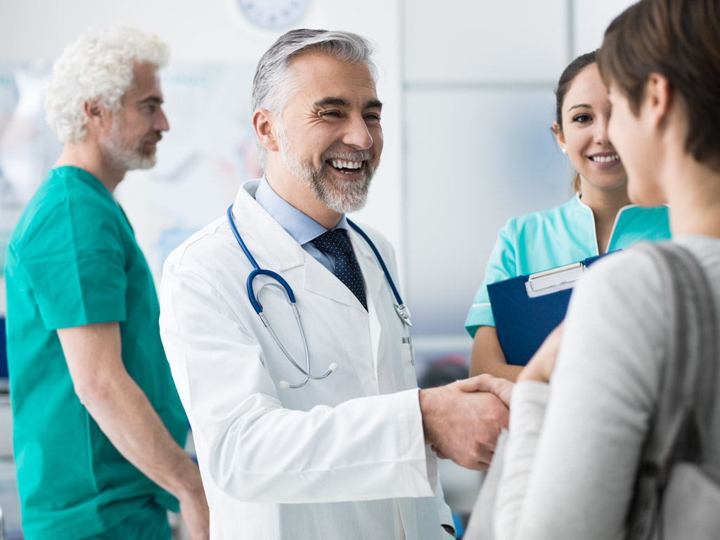 Freundlicher Arzt begrüßt Patientin mit Handschlag in der Arztpraxis. Medizinische Versorgung und Beratung im Krankenhaus.