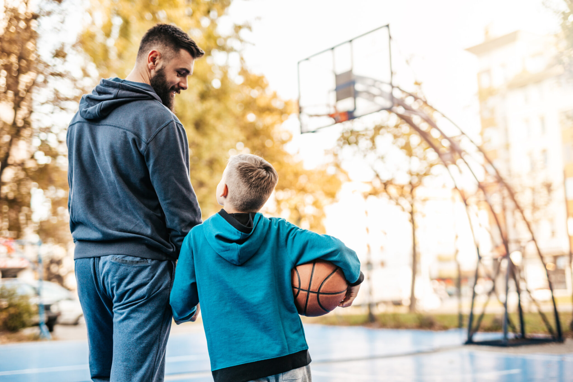 Erzieher und Junge mit Basketball stehen auf einem Sportplatz und schauen gemeinsam in die Zukunft.