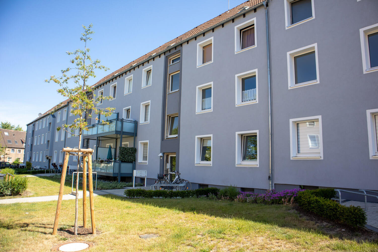 Dreigeschossiges Wohnhaus mit verglasten Balkonen und begrünter Außenanlage.