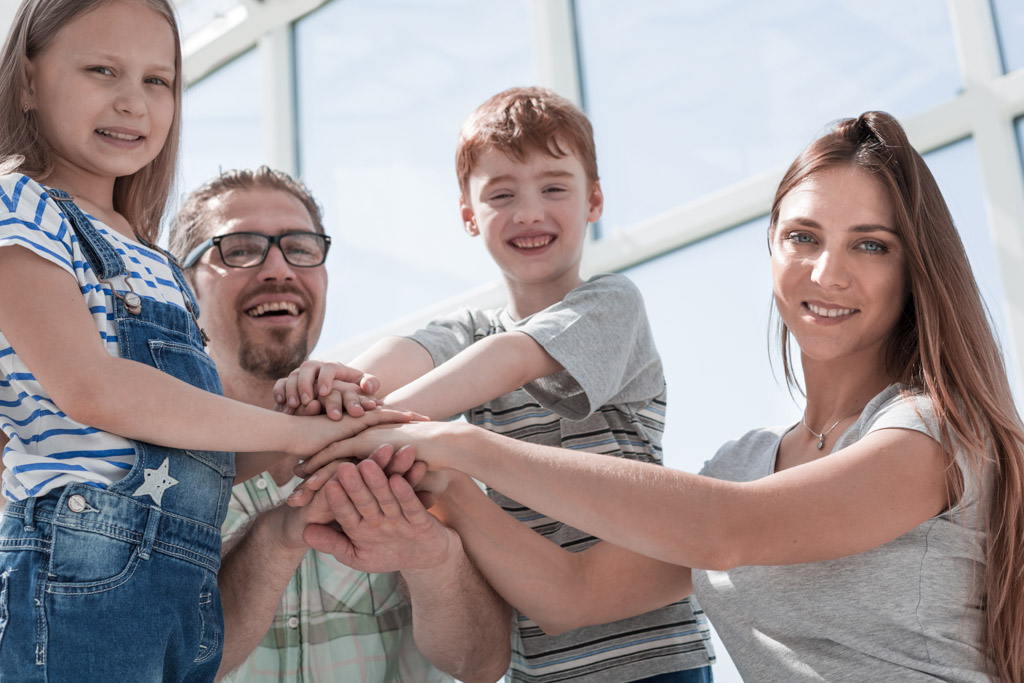 Eine Familie aus vier Personen steht Hand in Hand und strahlt Freude aus.