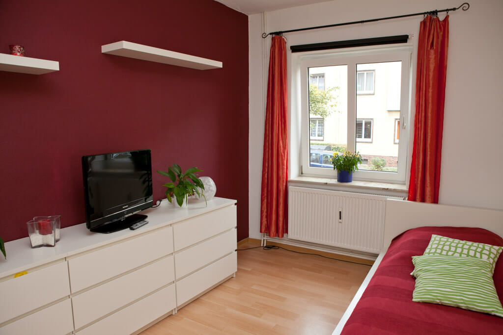 Gemütliches Schlafzimmer mit Bett, Fernseher und einem Fenster für natürliche Beleuchtung.