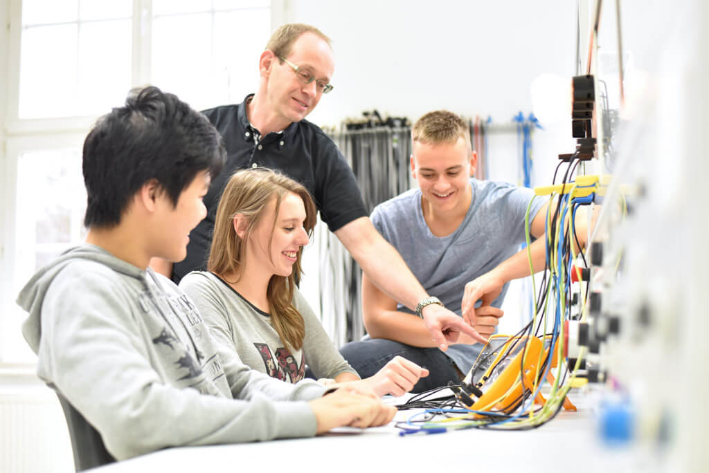 Drei Studenten tüfteln an Elektronik in einem Klassenzimmer.
